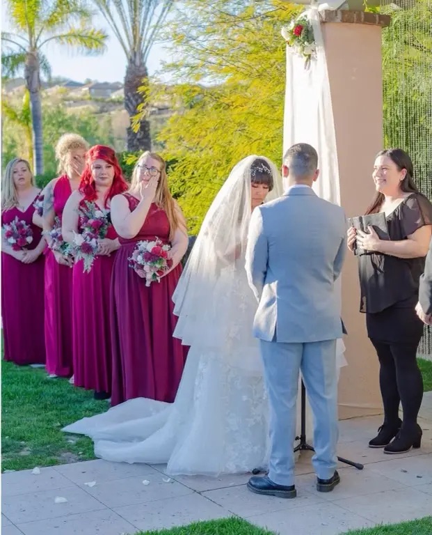Officiant reading a personalized ceremony script in front of floral arch and guests